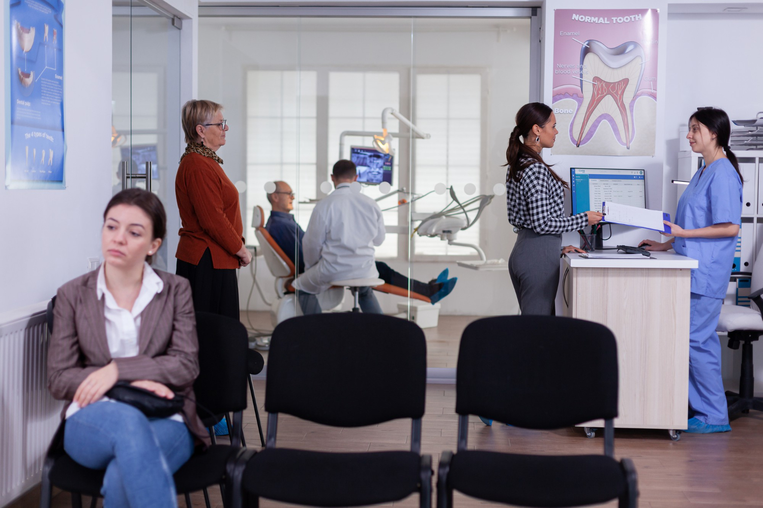Sala de espera de una clínica dental con pacientes y recepcionista atendiendo en el mostrador